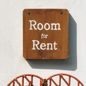 Wooden “Room for Rent” sign on white wall with teal framing and red decoration, symbolising the softening rental market